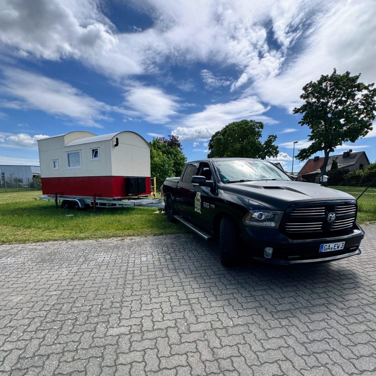 Seriengefertigt. Schwarzer Dodge RAM vor Tiny House mit rotem Streifen auf Trailer.
