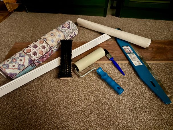 Tapeten, Pinsel Malerbürste und -rolle liegen mit einem Stück Laminat auf einem Teppich.
