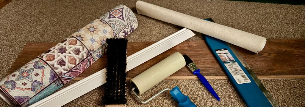 Tapeten, Pinsel Malerbürste und -rolle liegen mit einem Stück Laminat auf einem Teppich.