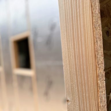 Nahaufnahme Holzbalken mit alukaschierter Dämmung im Hintergrund.