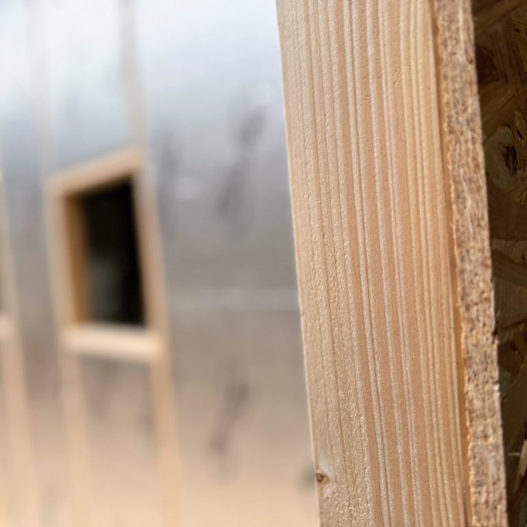 Seriengefertigt. Nahaufnahme Holzbalken mit alukaschierter Dämmung im Hintergrund.