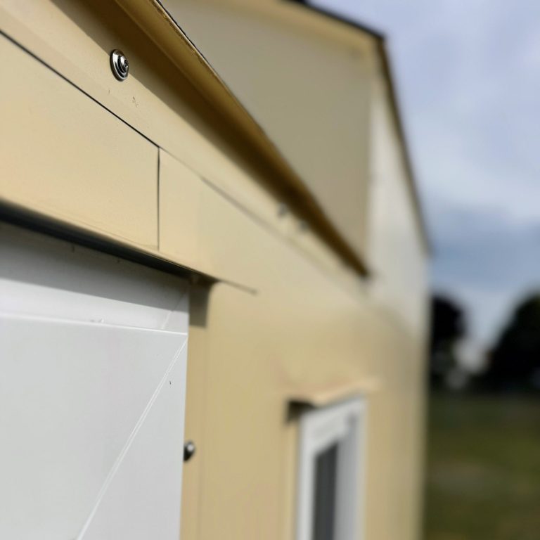 Seriengefertigt. Nahaufnahme Blechfassade mit Abtropfblechen über Tür.